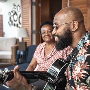 Man playing a guitar with an older woman watching in the background