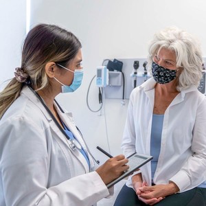 Doctor with mask is talking with a patient who is wearing a mask. 