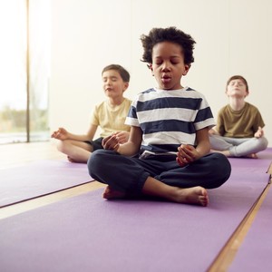 Group Of Children Sitting On Exercise Mats And Meditating In Yoga Studio