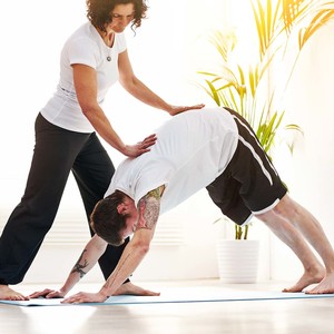 Female yoga instructor training a man to do downward dog pose during a fitness class in an exercise studio.