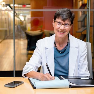 Dr. Helene Langevin writing in a notepad and smiling at a desk in an office. 
