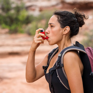 A young female takes a short break from her day hike to use her inhaler.