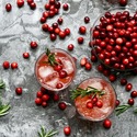 Whole cranberries in a bowl and placed within 2 drinks on a table.