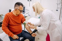 A seated middle aged man having blood drawn from a medical technician.