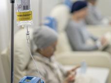 A chemotherapy bag hanging and a woman receiving treatment sitting in a chair.