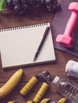 A banana, water bottle, hand grip strengthener, dumbbell, and tablet and pen on a table. 