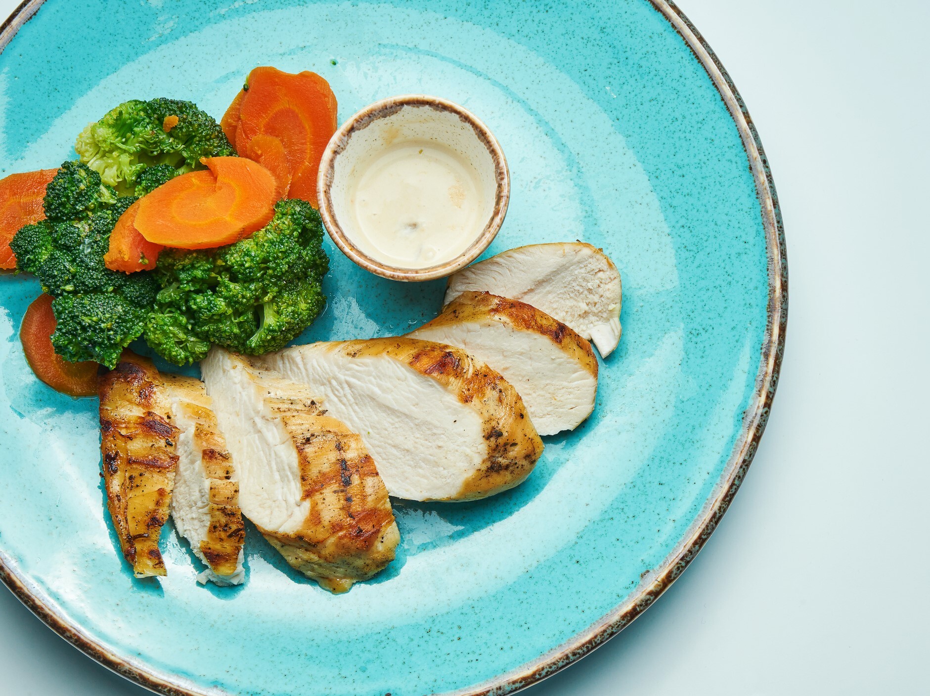 grilled chicken, broccoli, and carrots nicely arranged on a blue plate