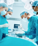 A group of four medical professionals wearing scrubs, gloves, and masks,  standing around a patient laying on an operating table.