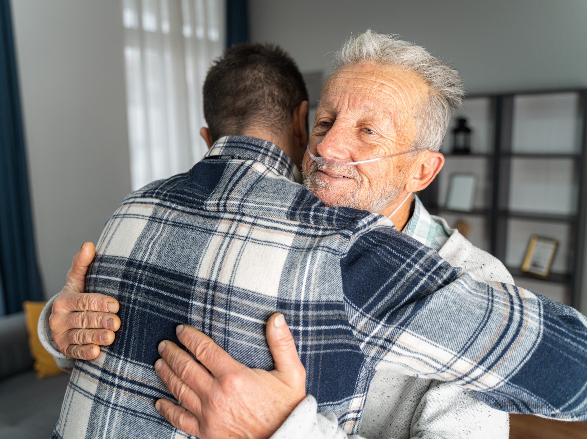 an older man with an oxygen tube in his nose hugs a younger man