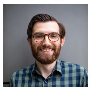 Professional headshot of Anthony Castanza, Ph.D. He's dressed in a flannel dress shirt against a gray background.