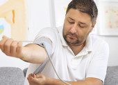 A man putting a blood pressure cuff on his arm at home.