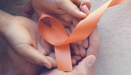A group of hands together holding an orange ribbon.