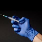 A blue-gloved hand holds a vaccine needle