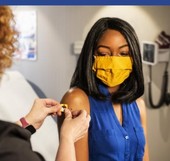 A woman in a cloth face mask receives a vaccine.