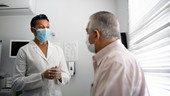 A patient speaks to his doctor. Both wear face masks.