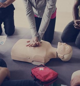 A group of people watching one person performing CPR on a dummy