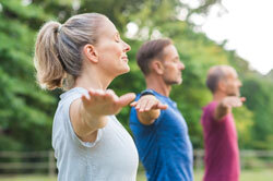 Group of adults stretching arms outdoors with eyes closed.