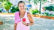 Image of a Hispanic woman outdoors smiling while holding a heart to her chest.