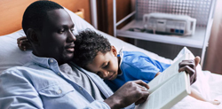 Father reads book to young son in hospital bed