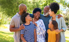 An intergenerational family with kids, parents, and grandparents embrace each other as they pose for a photo outside.