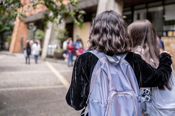 Rearview of two teenage students wearing backpacks and walking side by side into school.