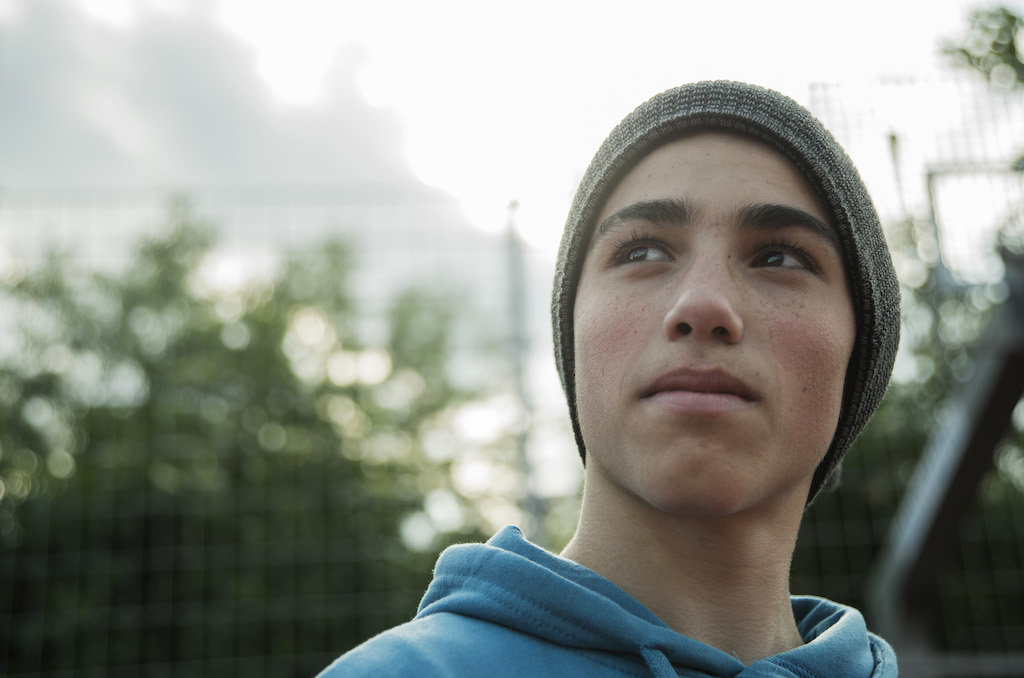 Teenage boy outside wearing a beanie cap and looking thoughtfully away from the camera.