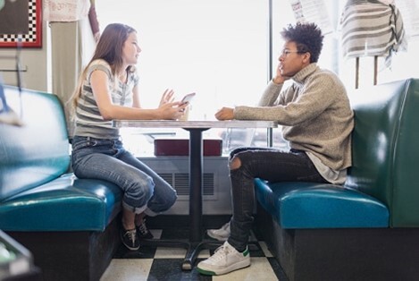 Two teens talking while sitting at a booth in a restaurant