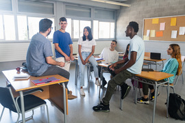 Diverse group of students with young male teacher sitting casually in a classroom and having a conversation.