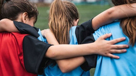 Rear view of three girls wearing sport uniforms standing and supporting each other.