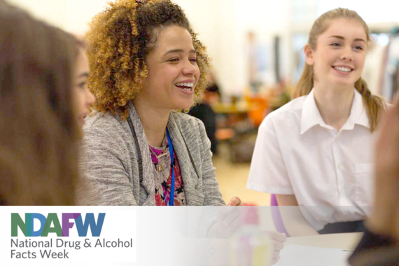 Young teacher sitting in a classroom and laughing with students; NDAFW logo lower left corner