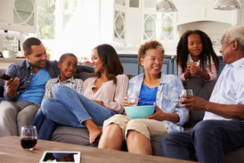 A family including parents, grandparents, a boy, and a girl sitting on a couch smiling.