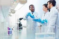 Young male scientist holding flask of liquid in a lab setting, discussing chemical reaction with another young male scientists.