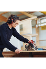 A woman uses a circular saw while wearing protective earmuffs.