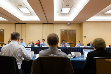 Panel of reviewers with laptops in a conference room.