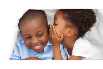 A young girl whispers into a boy's ear.