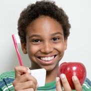 child with beautiful teeth and smile holding toothbrush, dental floss, and apple.