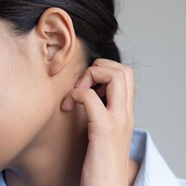 person scratching upper neck behind ear