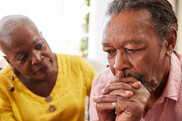 Elderly Black man and woman sitting together looking at each other with concern.