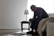 Older male sitting alone on bed