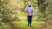 Senior woman hiking on a wooded path with COVID-19 face protection.