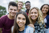 A diverse group of happy young adults standing together outside and facing the camera