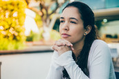 Stock photo of a young woman sitting outside looking away and leaning on her hands.