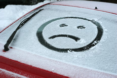 Sad face drawn in snow on a car windshield