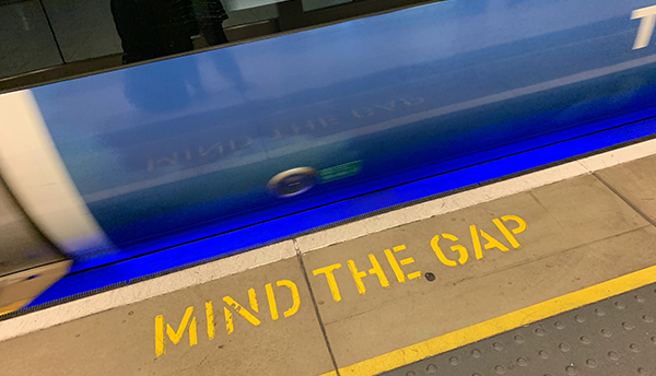 A subway platform says "Mind the Gap" in yellow on concrete.