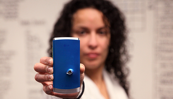 A woman displays a cellphone with a bullet hole in it (forensics).