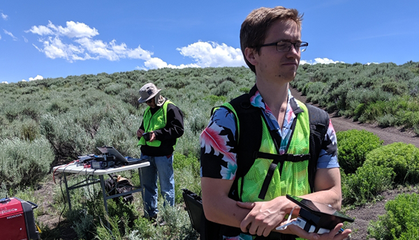 Hien Nguyen (PSCR) sets up test equipment at a table outdoors while Josh Hamel holds a test device nearby.