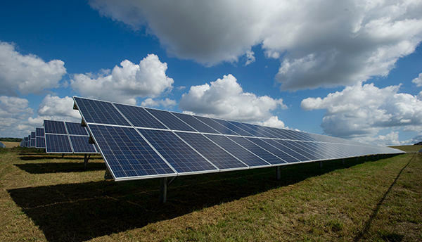 A solar array is mounted on the ground under a blue sky with clouds. 