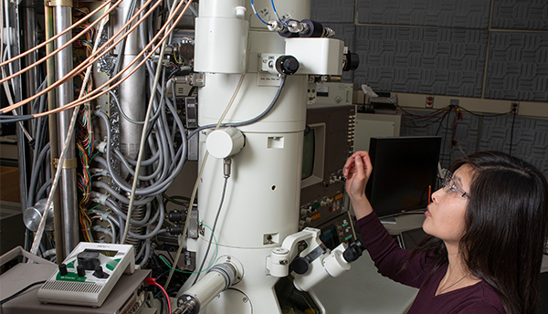 A researcher (June Lau) works on a white microscope with devices and wires attached.