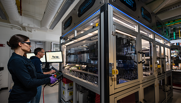 Two researchers program the robotic arm that operates within the boxlike structure of the NIST biofoundry.