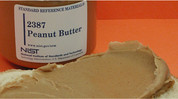 Jar labeled "Standard Reference Material: Peanut Butter" sits near a piece of bread with peanut butter on it.